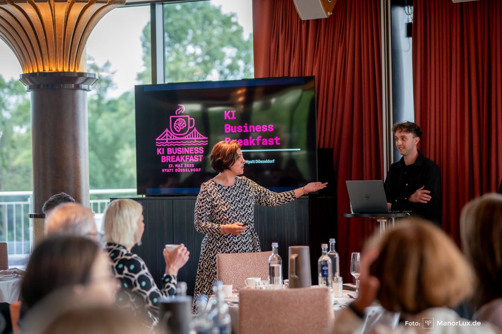 KI Business Breakfast. Speaker Niklas und Moderatorin Martha stehen in einem Raum voller Gäste an kleinen Tischgruppen im Hyatt Düsseldorf